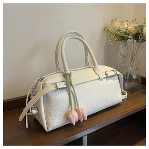 Close-up of white Boston handbag with pink tulip charm on a rustic wooden shelf