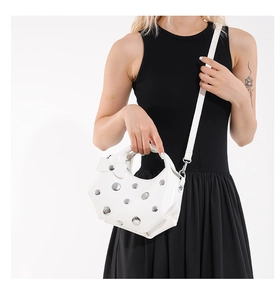 Detail of white glossy leather bag featuring silver metal rivets and a chic bow accent
