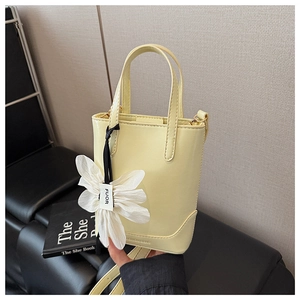 Detail of a light yellow leather bucket bag with a large white 3D flower petal charm