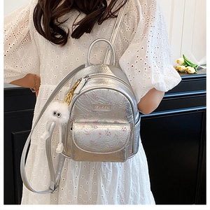 Close-up of silver mini backpack with floral pattern and white plush keychain on model