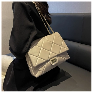 Beige quilted chain bag on shoulder with black blazer and minimalist interior backdrop