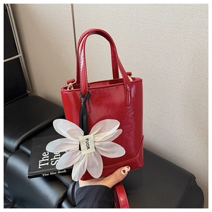 Detail of red patent leather mini bucket bag with a white organza flower charm