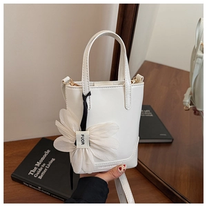 Detail of white mini bucket bag featuring a large soft fabric flower charm on wooden table