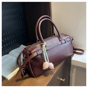 Detail of dark brown leather handbag with tulip charm on a rustic wooden desk