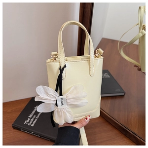Detail of pale yellow bucket bag with floral charm and detachable strap on a wood table