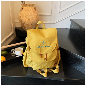 Détail d'un sac à dos en nylon jaune avec broderie Take it Easy sur un escalier noir