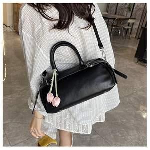 Detail of black litchi texture boston bag with pink tulip pendant and slim shoulder strap