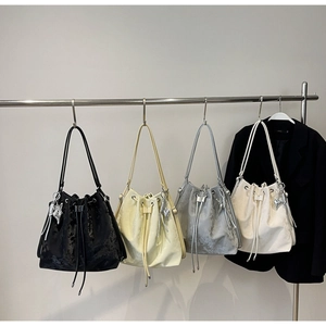 Detail showing four drawstring bucket bags with metal pendants in black, yellow, grey and white