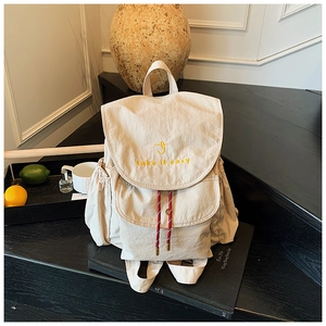 Détail d'un sac à dos en nylon beige avec broderie et cordon de serrage rayé décoratif