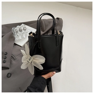 Detail of black glossy mini bucket bag featuring a large white flower charm with dual handles