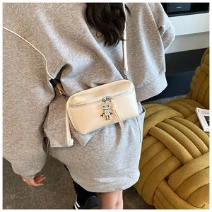 Close-up of cream leather crossbody mini box bag featuring a cute metal robot charm detail