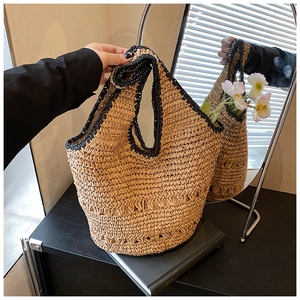 Detail of hand-woven straw tote bag with black contrast handles and large bucket design