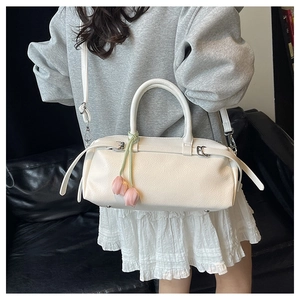 Close-up of white pebble leather Boston bag featuring a cute pink tulip charm and strap