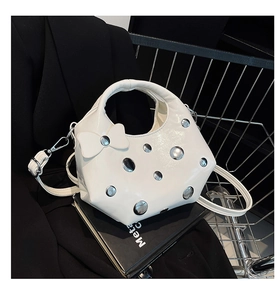 Détail d'un sac à main blanc brillant avec rivets argentés et nœud décoratif