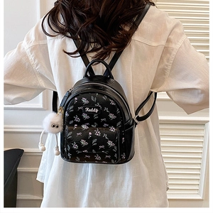 Detail of black floral mini backpack with plush pendant and brand label on white shirt