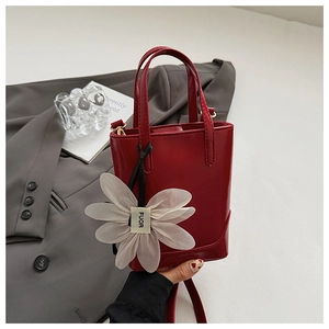 Detail of red patent leather bucket bag with white floral charm on grey blazer