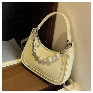 Détail du sac hobo beige avec chaîne décorative en cœur et perles sur surface en bois