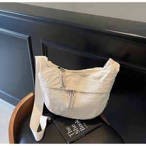 Detail of a creamy white crescent canvas crossbody bag with pleated texture on a leather seat