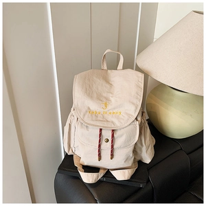 Détail macro du sac à dos en nylon beige avec broderie jaune et cordons contrastés