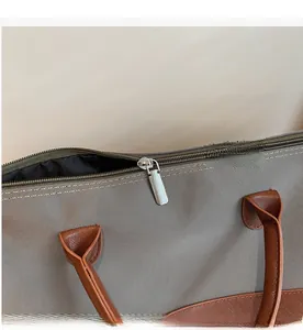 Détail de la fermeture éclair argentée et poignée en cuir brun sur sac gris