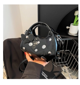 Détail du sac en cuir verni noir avec rivets argentés et nœud papillon élégant