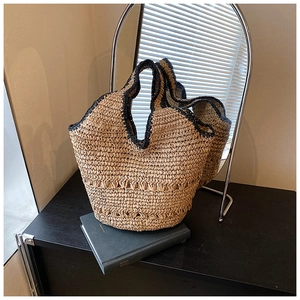 Detail view of woven straw tote bag featuring contrast black trim and wave edge design