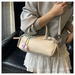Detail of a beige pebbled leather Boston bag with a purple tulip charm on a model