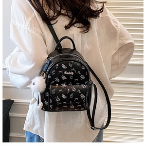 Dettaglio di un mini zaino nero con stampa floreale, logo Keddy e ciondolo in peluche bianco