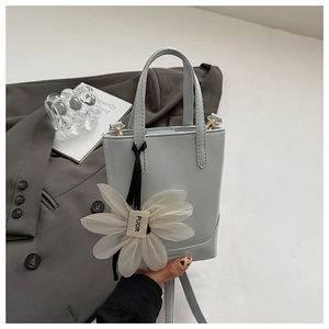 Detail of light blue bucket bag with white daisy charm and metal shoulder strap hardware