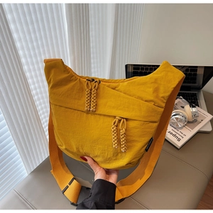Detail of yellow canvas crossbody bag with woven zipper pull and adjustable buckle strap