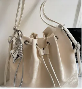 Detail of a creamy white drawstring bucket bag with litchi texture and silver heart charm