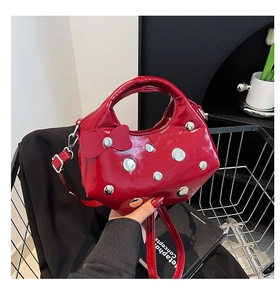 Gros plan d'un sac seau en cuir verni rouge avec clous argentés et détail de nœud décoratif