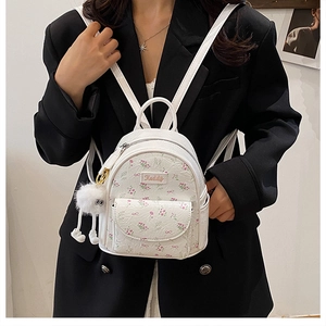 Detail of white mini backpack with floral bow patterns and a soft white pompom charm