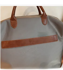 Gros plan du tissu gris avec poignées en cuir marron et logo Noco sur le sac cabas