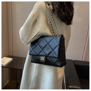 Detail of black quilted leather shoulder bag with gold clasp worn over a white coat