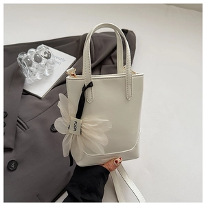Detail of white mini bucket bag featuring a 3D floral charm and smooth PU leather