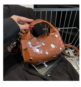 Détail d'un sac à main marron brillant avec des rivets argentés et nœud métallique