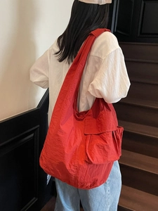 Large red nylon tote bag with functional pockets and wide shoulder straps worn by model