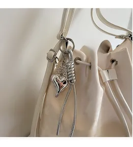 Detail of silver heart charm with butterfly and tassel on beige bucket bag