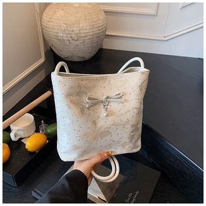 Detail of cream white bag featuring bow decoration, pearl charm, and floral patterns