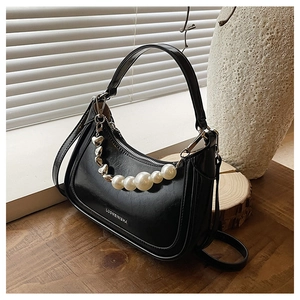 Détail du sac noir avec chaîne de perles et pendentifs cœur sur support bois
