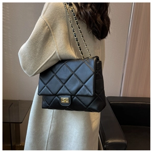 Close-up of black quilted shoulder bag with gold chain strap on light beige coat