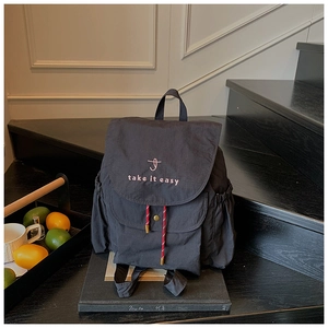 Détail d'un sac à dos en nylon noir avec broderie rose 'take it easy' et cordon à motif