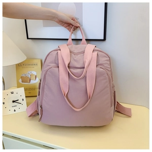 Detalle de mochila de nailon rosa con cremallera, bolsillo frontal y asas de cinta