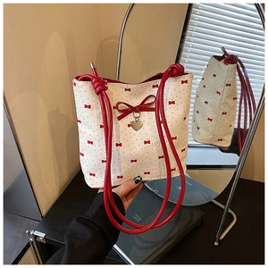 Close-up of bow shoulder bag with red rope handle and heart pendant on mirror surface