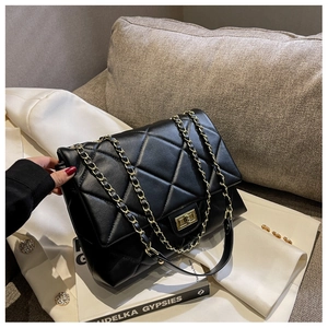 Detailed view of black quilted flap bag with golden twist lock on white blazer