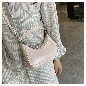Detail of pink crescent bag featuring decorative pearl chain and smooth patent leather