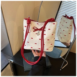 Close-up of white leather bag with red bows, heart charm, and knotted rope shoulder strap