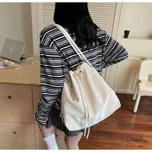 Detail of a large white bucket bag featuring drawstring closure and side silver zipper accent