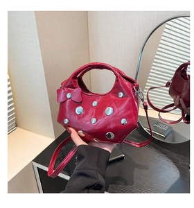 Détail du sac demi-lune rouge avec nœud et rivets argentés tenu à la main